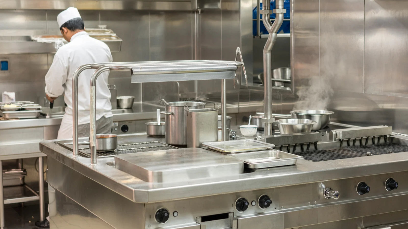 Commercial kitchen with stainless steel appliances and a chef in uniform.